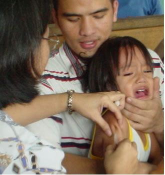 Nurse gives a crying child an immunization shot while man holds and comforts her