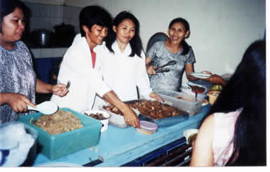 Four Philippine women smiling as they lay out food for children