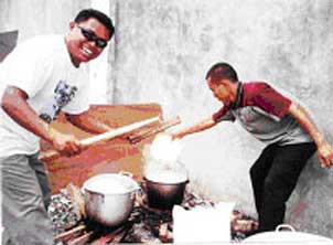 Two men, happily cooking rice in large open pots.
